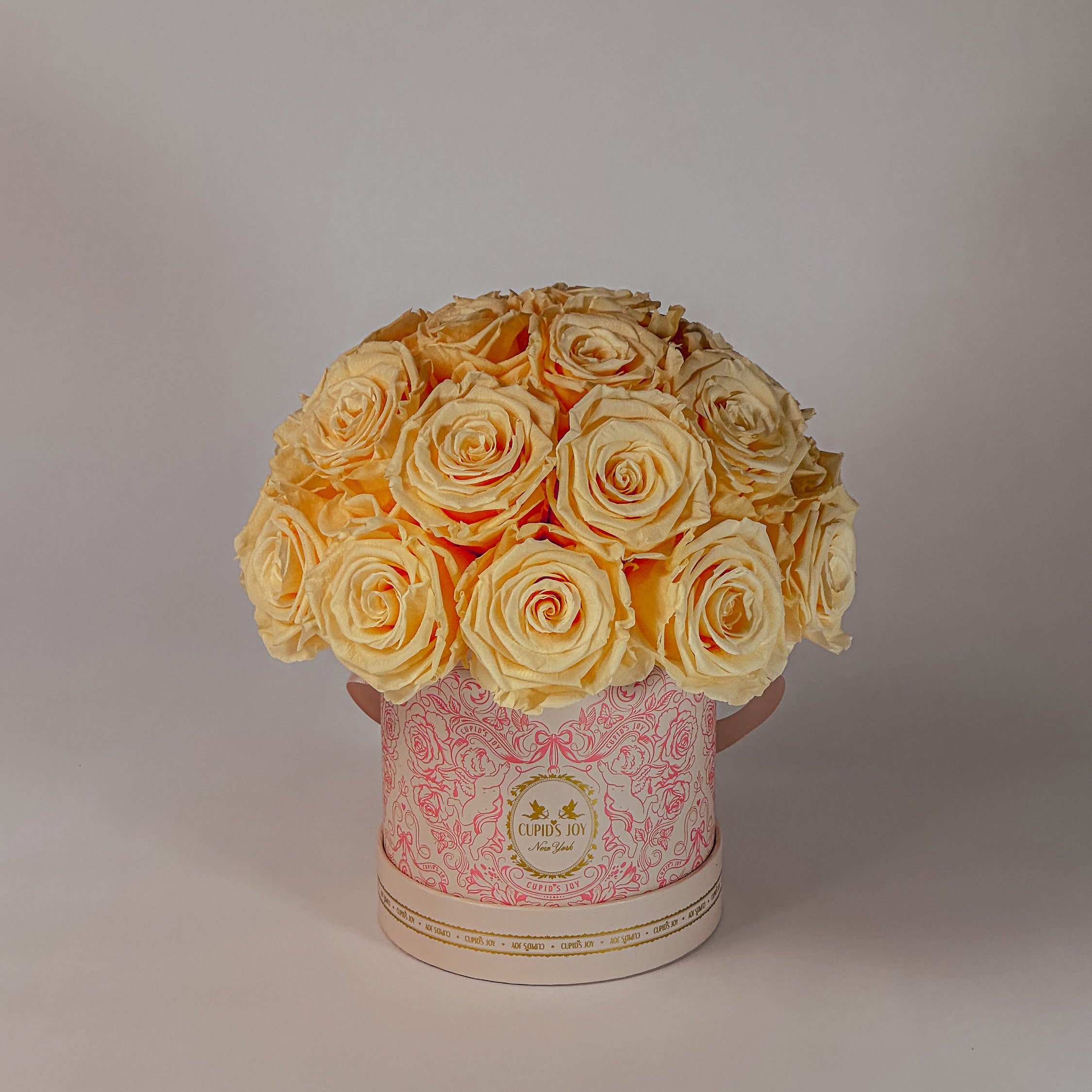 Bouquet of yellow forever roses in a decorative pink box on a light gray background