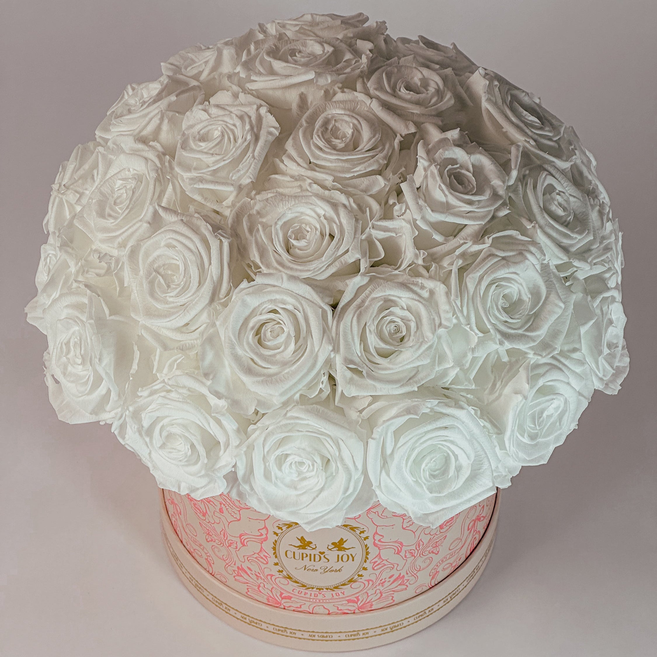 White roses in a round box with a Cupid's Joy brand logo on a light gray background