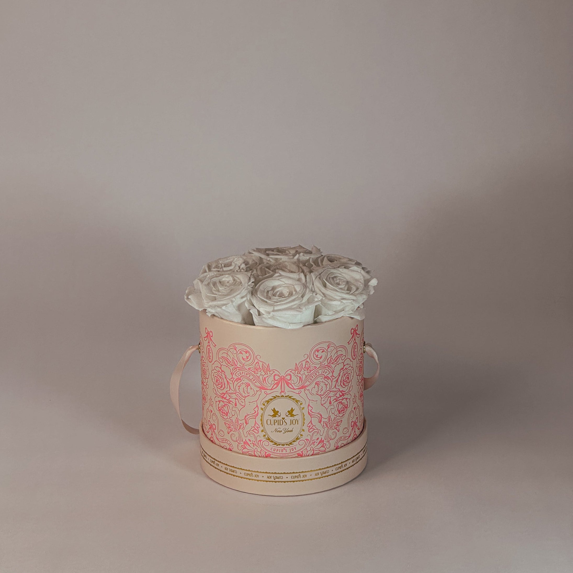 Cupid-motif box by Cupid's Joy with white eternal roses on a plain background