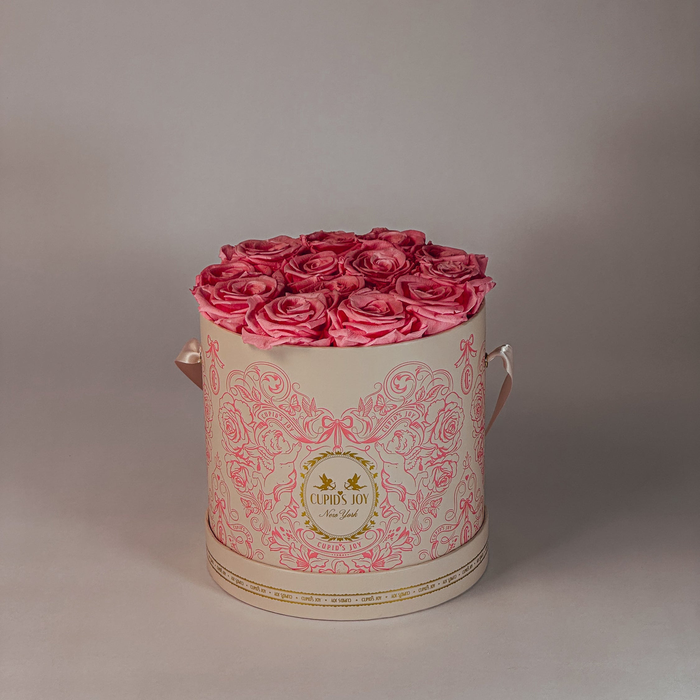Round cupid-motif box with pink forever roses on a plain background