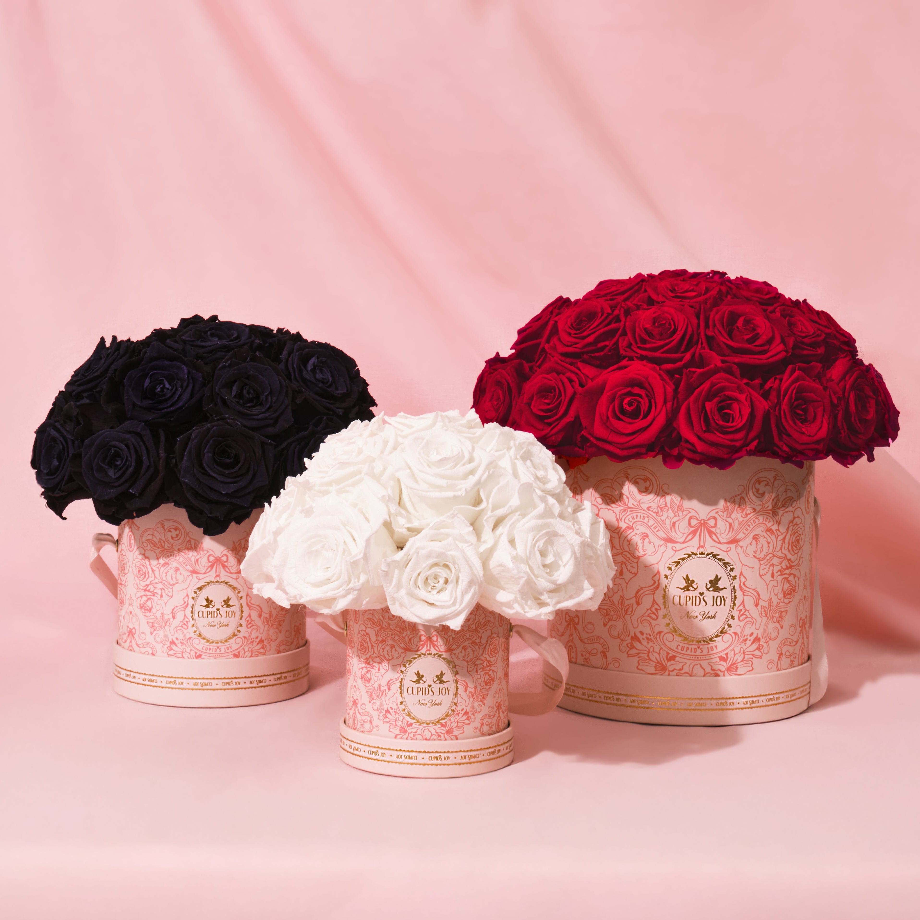 Three flower arrangements in black, white, and red in decorative boxes on a pink background